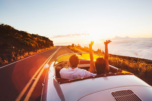 زوج خوشبختی که در جاده کانتری به سمت غروب خورشید با ماشین کلاسیک کلاسیک رانندگی می کنند
