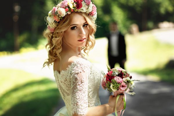 عروس عاطفی خندان و زیبا با لباس سفید قدیمی در نمای نزدیک تاج گل