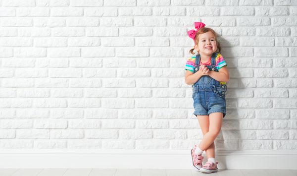 دختر بچه شادی که به دیوار آجری خالی می خندد