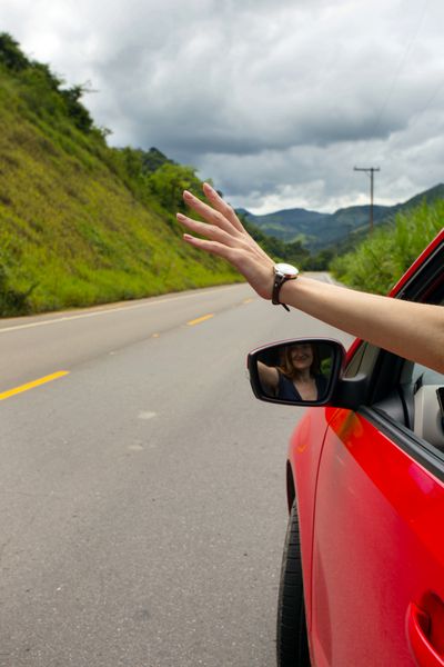 دست دختری که از ماشین در پس‌زمینه‌ای از کوه‌ها برزیل نگاه می‌کند