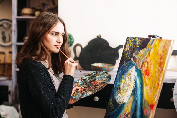 نقاش متفکر خلاق یک تصویر رنگارنگ ترسیم می کند نمای نزدیک از فرآیند نقاشی در کارگاه هنری نقاش مثبت زن خلاق در تصویر انتزاعی استودیو خود نقاشی می کند