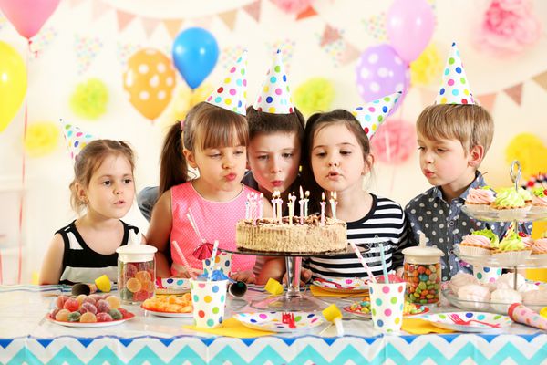 گروه شاد کودکانی که در جشن تولد روی کیک شمع می افروزند