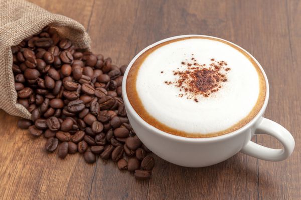 کاپوچینو قهوه و دانه های قهوه در زمینه چوبی