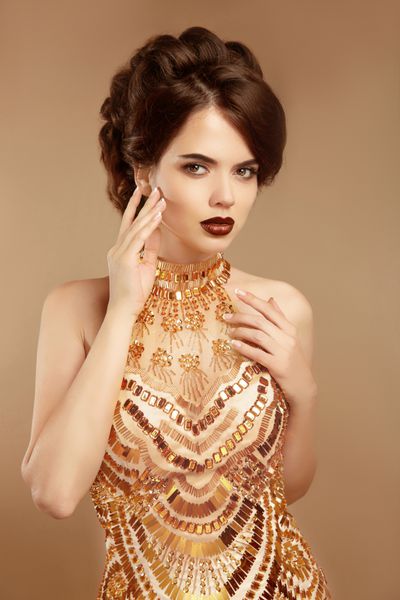 آرایش زیبایی مدل مو زن مد با لباس طلایی جدا شده در زمینه بژ ناخن های مانیکور شده سبک Vogue