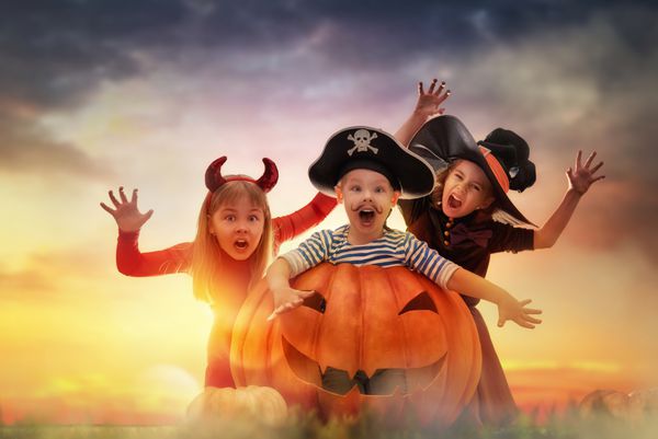 برادر و دو خواهر در هالووین مبارک بچه های خنده دار در لباس های کارناوال در فضای باز کودکان شاد و کدو تنبل در پس زمینه غروب آفتاب
