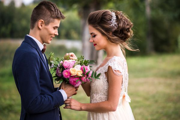 عروس و داماد جوان و زیبا که دسته گل عروسی را در دست دارند تابستان