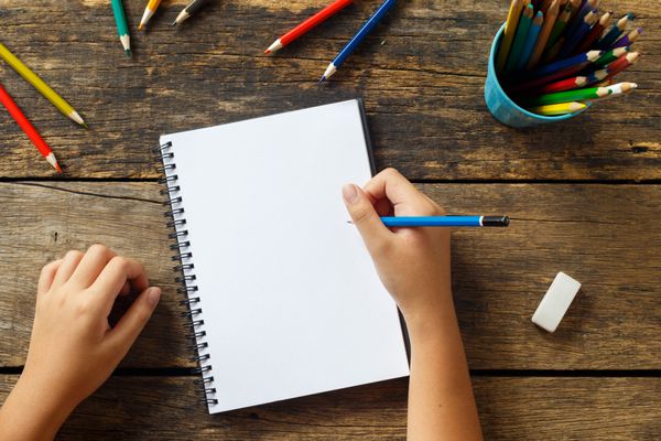 نقاشی دست دختر بچه کاغذ خالی و مدادهای رنگارنگ روی میز چوبی قدیمی