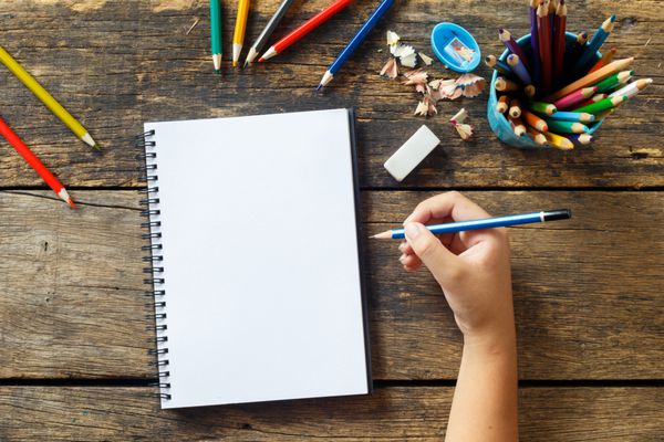 نقاشی دست دختر بچه کاغذ خالی و مدادهای رنگارنگ روی میز چوبی قدیمی
