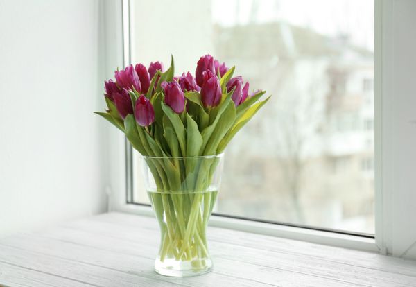 گلدان شیشه ای با دسته گل لاله های زیبا روی طاقچه