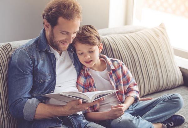 پدر و پسر در حال خواندن کتاب و لبخند زدن در حالی که با هم در خانه می گذرانند