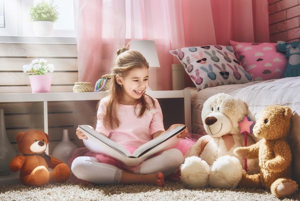 دختر بچه ناز در خانه در حال خواندن کتاب است کودک دوست داشتنی خنده دار در حال تفریح در اتاق بچه ها