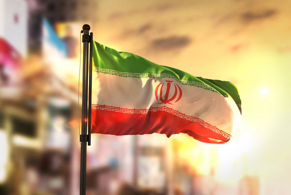 پرچم ایران در مقابل پس‌زمینه تار شهر در رندر سه‌بعدی نور پس‌زمینه طلوع آفتاب