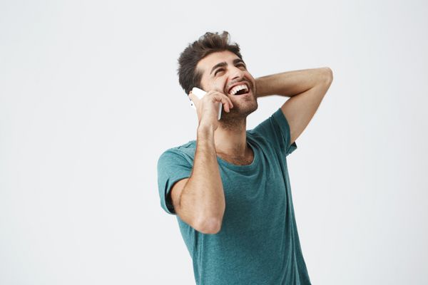 مرد جوان شاد هنگام صحبت با تلفن احساس هیجان شادی و خنده دارد هیپستر شیک در حال برقراری ارتباط با دوست دخترش از طریق تلفن هوشمند با لبخند