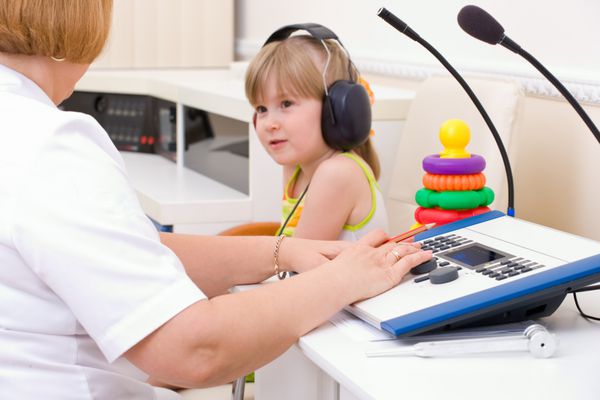 پزشک شنوایی شناس گوش دختر را روی تجهیزات پزشکی آزمایش می کند