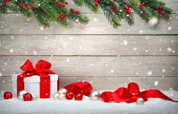 پس زمینه چوبی کریسمس با جعبه هدیه سفید پاپیون و روبان قرمز چوب دستی شاخه های صنوبر و برف