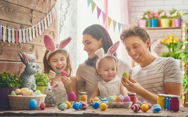 مادر پدر و دختر در حال رنگ کردن تخم مرغ هستند خانواده شاد در حال آماده شدن برای عید پاک هستند دختر بچه ناز با گوش های اسم حیوان دست اموز