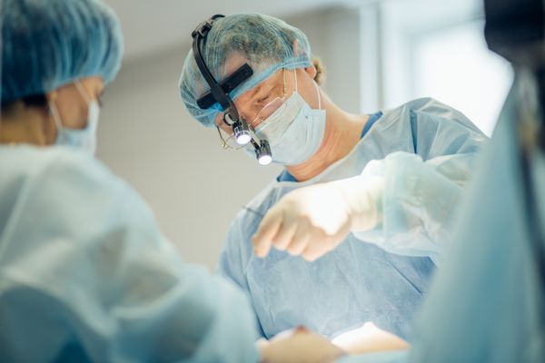 جراح در حال انجام جراحی زیبایی سینه ها در اتاق عمل بیمارستان جراح با ماسک با پوشیدن لوپ های جراحی در طول عمل پزشکی بزرگ کردن سینه بزرگ کردن بزرگ کردن سینه