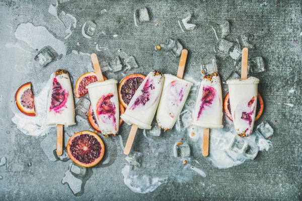 دسر تابستانی سالم بستنی‌های پرتقال خونی ماست و گرانولا روی تکه‌های یخ روی زمینه بتونی خاکستری نمای بالا ترکیب افقی تغذیه تمیز رژیم غذایی مفهوم کاهش وزن