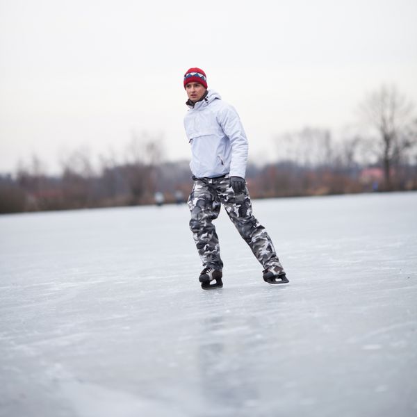 مرد جوان خوش‌تیپ در حال اسکیت روی یخ در بیرون از حوضچه در یک روز ابری زمستانی تصویر رنگی DOF کم عمق