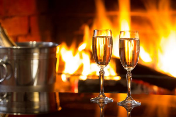 دو لیوان شراب سفید درخشان و سطل یخ جلوی شومینه گرم فضای جادویی رمانتیک و دنج و آرام در نزدیکی آتش مفهوم روز ولنتاین