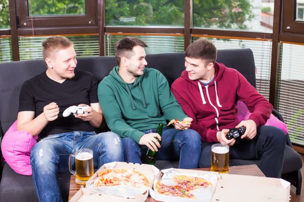 مردان جوان آبجو می نوشند پیتزا می خورند و کنسول بازی می کنند