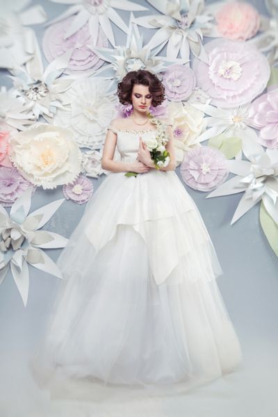 عروس جوان زیبا با لباسی زیبا روی پس زمینه گل های کاغذی بزرگ