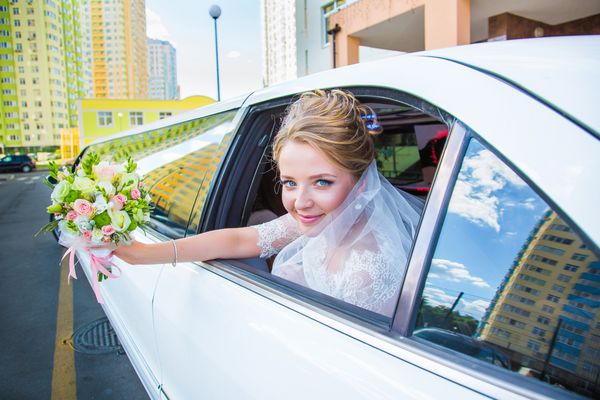 عروس زیبا و جذاب با لباس عروس دسته گل لیموزین را تکان می دهد