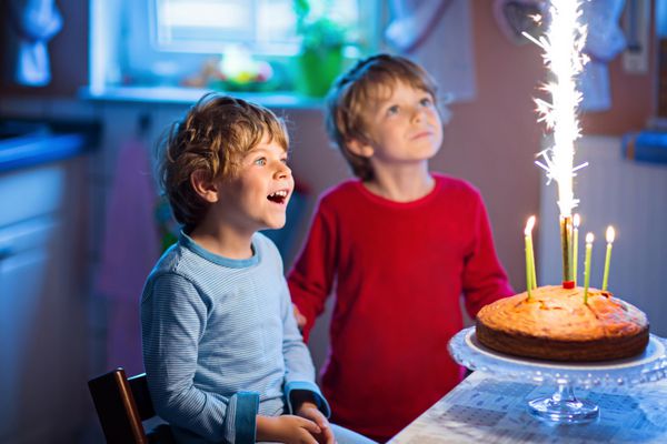 دوقلوهای پسر بچه کوچک در حال جشن تولد و دمیدن شمع روی کیک