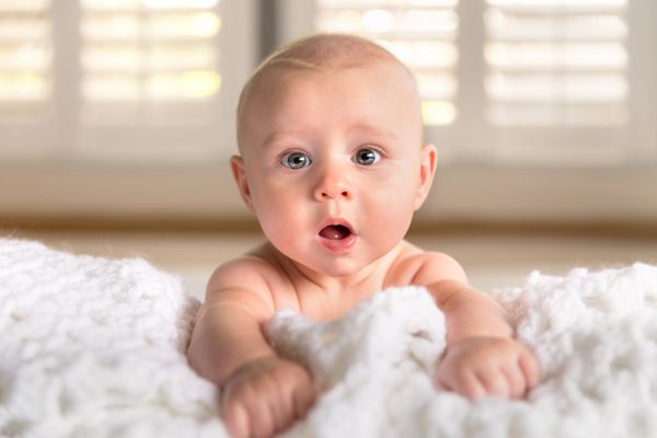 تعجب خنده دار بامزه گونه های چاق پف کرده چشمان آبی درشت کودک نوزاد در گهواره