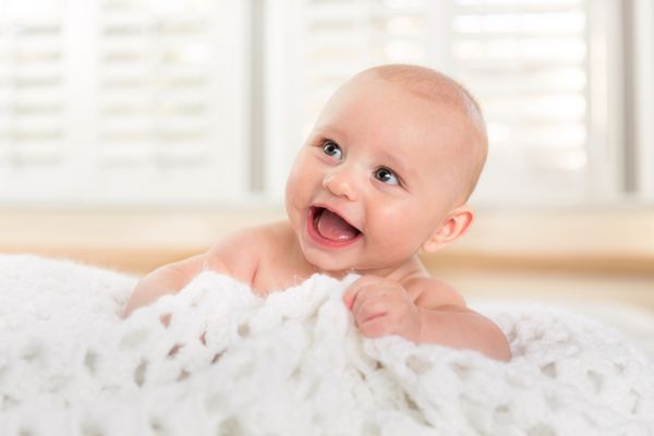 لبخند بزرگ و خنده ای از نوزادی که بعد از حمام با پتو بازی می کند معصوم خالص است