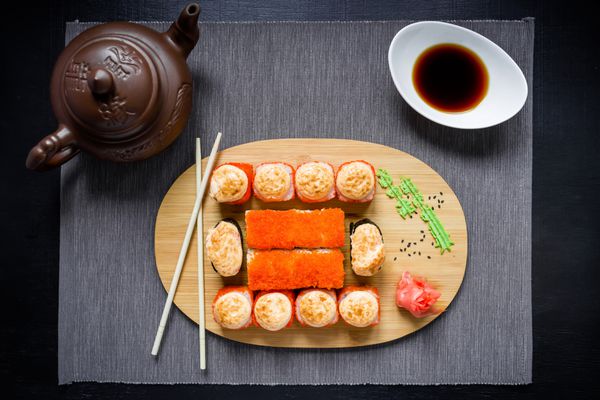 مجموعه ای از رول سوشی سس سویا فنجان چای و چاپستیک روی یک سفره خاکستری نمای بالا تخت دراز کشید غذاهای سنتی ژاپنی