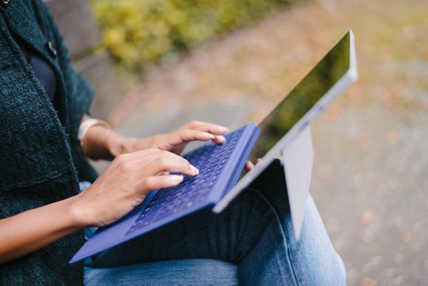 نمای نزدیک از زنی که روی یک لپ تاپ قابل تبدیل به تبلت در فضای باز پارک در پاییز کار می کند