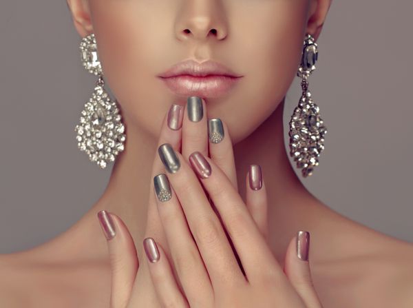 مدل دختر زیبا با مانیکور متالیک نقره ای صورتی و خاکستری روی ناخن آرایش مد و لوازم آرایشی جواهرات براق الماس نقره بزرگ گوشواره