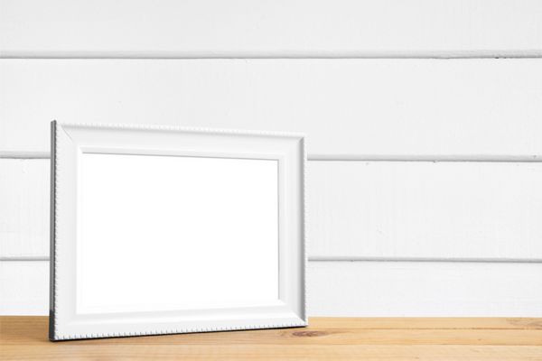 قاب عکس سفید روی میز چوبی در اتاق دیواری چوبی سفید قرار داده شده است