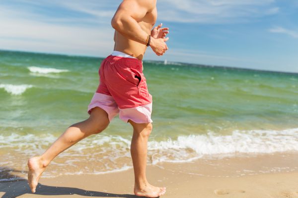 مرد شادی که در امتداد ساحل تابستانی می دود