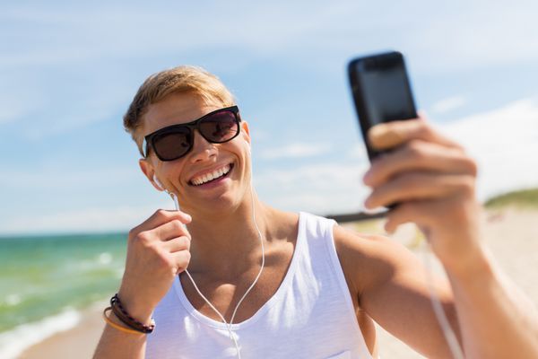 مردی با گوشی هوشمند در ساحل تابستانی سلفی می گیرد