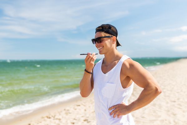 مرد خندان با تلفن هوشمند در ساحل تابستانی تماس می گیرد