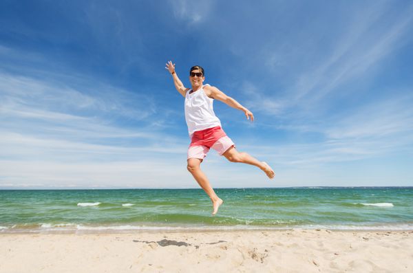 مرد جوان خندان در حال پریدن در ساحل تابستانی