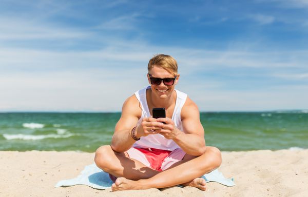 مرد جوان خندان با گوشی هوشمند در ساحل