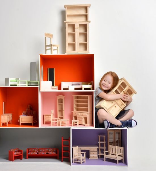 بچه دختر بچه مو قرمز در حال بازی با خانه عروسک پر شده با اسباب بازی های کوچک مبلمان