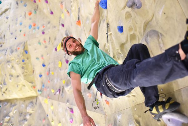 گلکلیچر اسپورتلر در کوهنورد Einer Kletterhalle که به دیوار آویزان شده و لبخند می زند