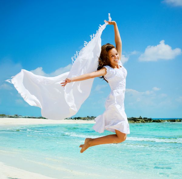 دختر زیبا با شال سفید پریدن در ساحل مسافرت و تعطیلات مفهوم آزادی