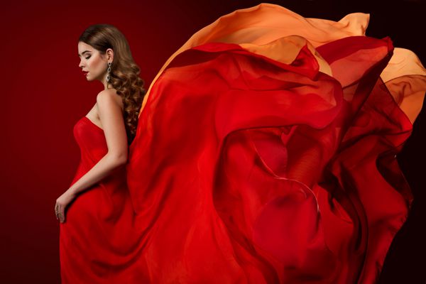 زن مدل مد لباس است در اهتزاز لباس شب قرمز دختر زیبا و پیچش پارچه ابریشم پرواز