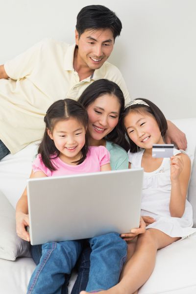 خانواده شاد از چهار نفر در حال خرید آنلاین از طریق لپ تاپ و کارت اعتباری در خانه هستند