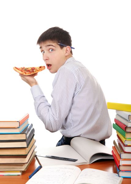 دانش آموز گرسنه مخفیانه در حال خوردن یک پیتزا در میز کار مدرسه