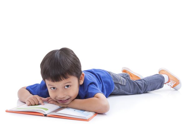 پسر کوچک خواندن کتاب با دروغ گفتن بر روی زمین