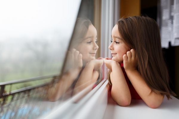 دختر کوچک زیبا لبخند زدن و تماشای پنجره یک کودک به پنجره نگاه می کند دختر جوان به دنبال پنجره پرتره از بچه خوش شانس دروغ در پنجره ی پنجره است