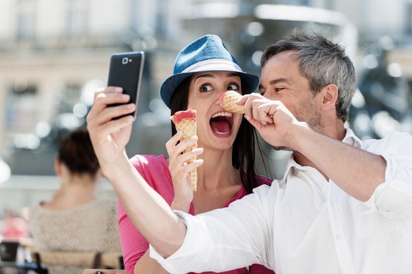 پرتره از یک زن و شوهر لبخند خوردن بستنی و داشتن سرگرم کننده در شهرستان مرد موهای خاکستری با ریش گرفتن تلفن همراه خود را می گیرد آنها چهره های خنده دار را می سازند