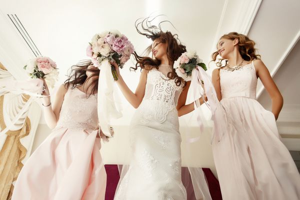 عروس و bridesmaids با دسته عروسی بر روی تخت در اتاق هتل پرش می کند
