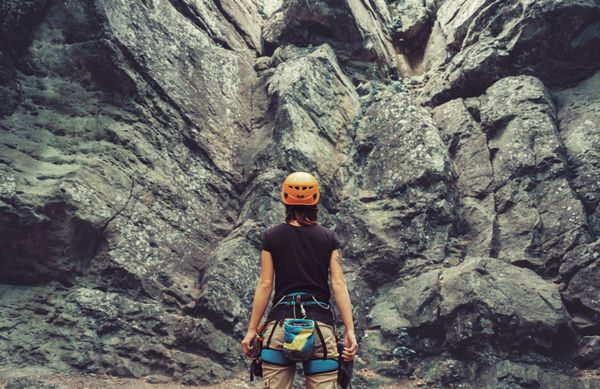 زن جوان پوشیدن در تجهیزات کوهنوردی ایستاده در مقابل یک فضای بیرون سنگ و آماده شدن برای صعود دید عقب